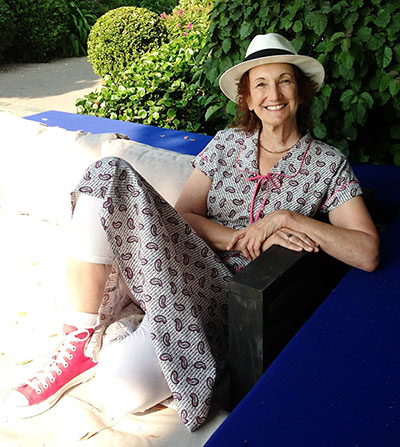 Photo of Sonya Sones kicking back on a porch in a blue folksy dress, red high-top sneakers, and a Panama hat from her webpage